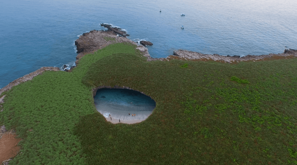 Vista aérea de la Playa Escondida en las Islas Marietas, rodeada de vegetación y costas rocosas junto al mar.