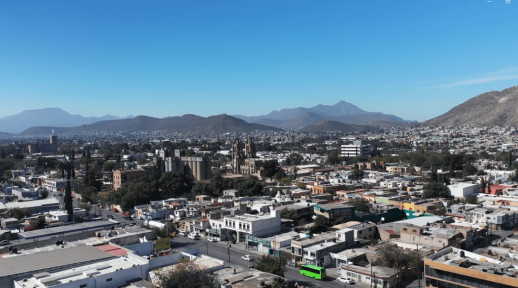 Vista aérea de Saltillo, Coahuila, con edificios del centro, una catedral y montañas al fondo bajo un cielo despejado