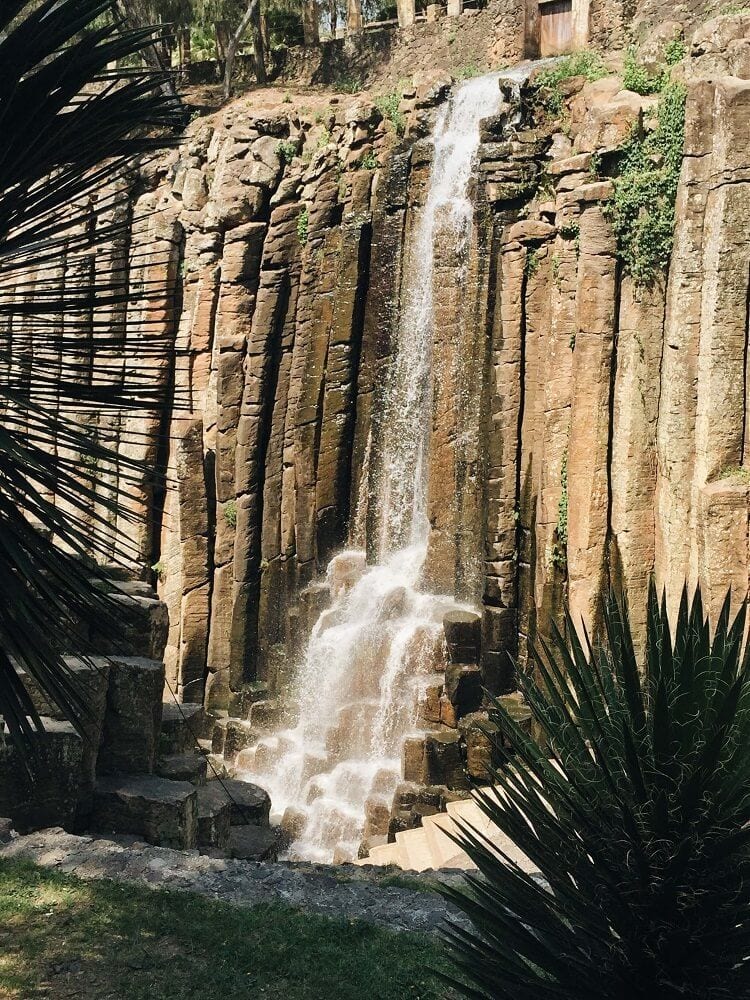 Cascada sobre las columnas de roca de los Prismas Basálticos en Huasca de Ocampo, Hidalgo, rodeada de vegetación.