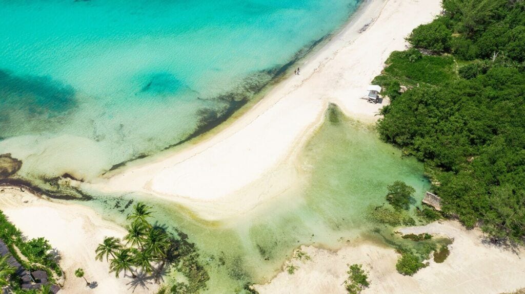 Vista aérea de una playa en Playa del Carmen, con arena blanca, aguas turquesas, palmeras y vegetación tropical.